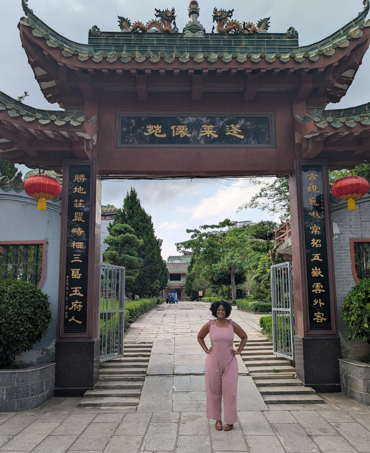 Kristen wearing The Icon Dusty Rose Jumpsuit in front of a Chinese-style gate, designed for a fuller bust